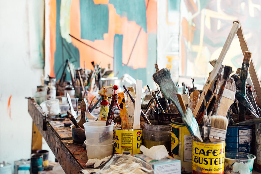 Cluttered artist workspace with paint brushes and supplies