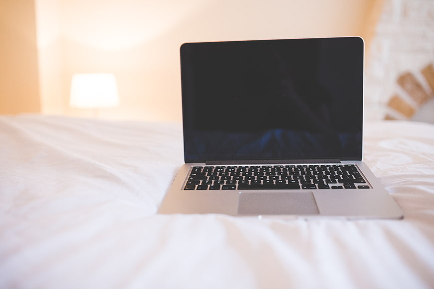 Silver laptop on white bed sheets in bright bedroom