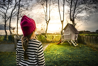Child in Pink Beanie Looking at Playhouse at Sunset