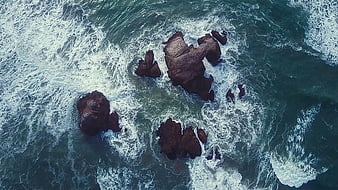 Aerial View of Ocean Waves Crashing on Dark Rocks