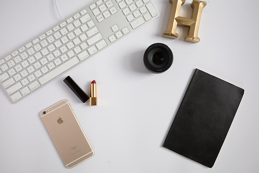 Flat lay of workspace with gold iPhone, lipstick, and camera lens