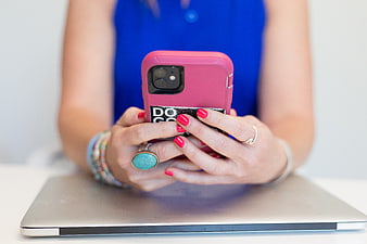 Woman holding pink smartphone over closed laptop