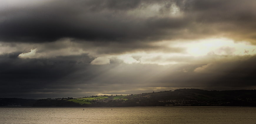 Dramatic sunbeams breaking through clouds over coastal landscape