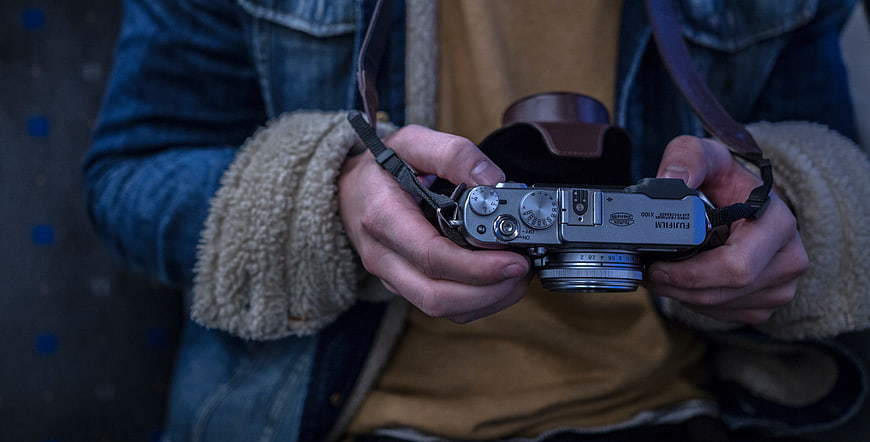 Close-up of hands holding a silver Fujifilm X100 camera