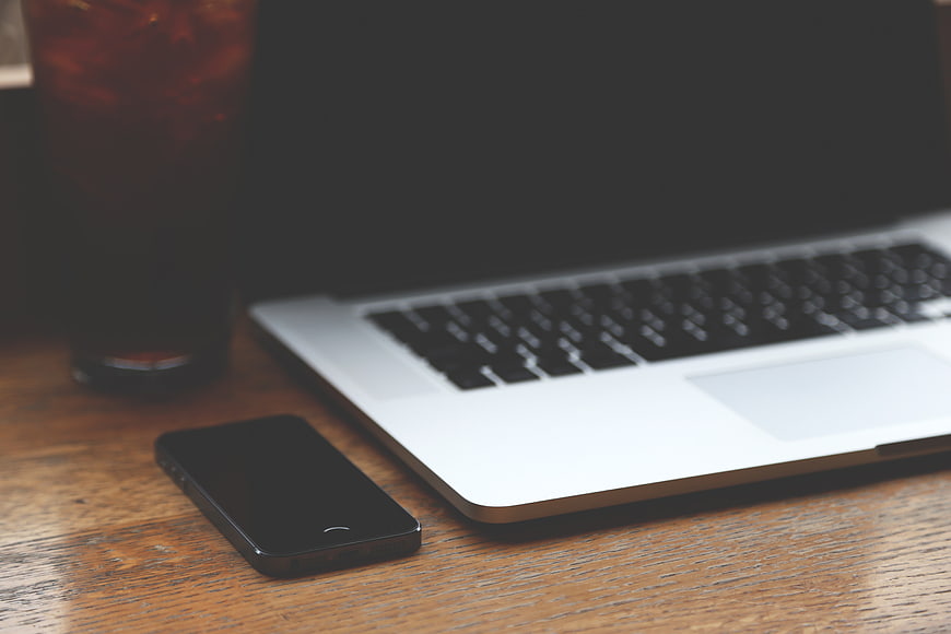 Laptop, smartphone, and iced coffee on wooden desk workspace