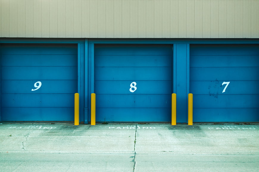 Blue industrial garage doors with yellow bollards and parking numbers