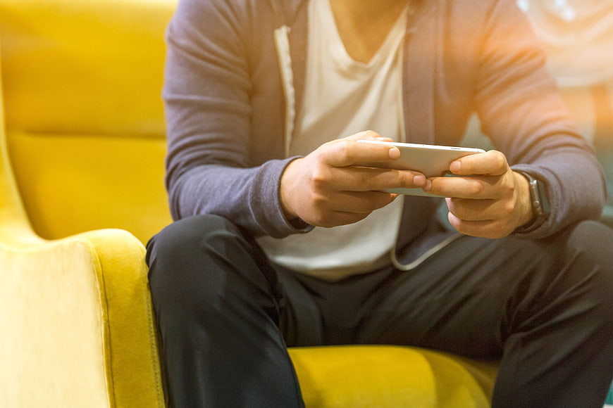 Man Playing Mobile Game on Smartphone Sitting on Yellow Sofa