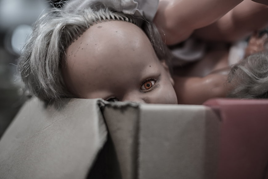 Close-up of creepy doll peeking over cardboard box edge