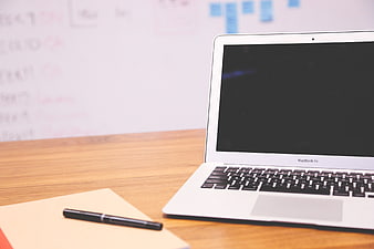 MacBook Air on wooden desk with notebook and pen