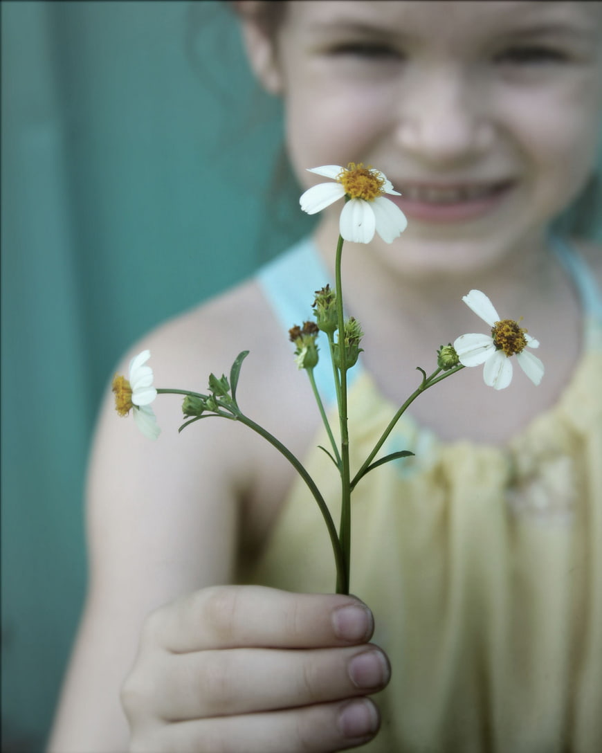 Child holding white wildflowers with blurred smiling face