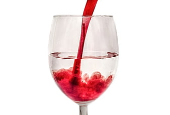 Red liquid pouring into a clear wine glass on white background