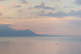 Serene Sunset Over Calm Ocean with Distant Mountains and Boat