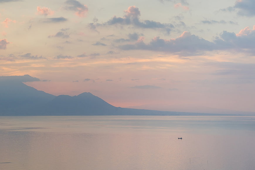 Serene Sunset Over Calm Ocean with Distant Mountains and Boat