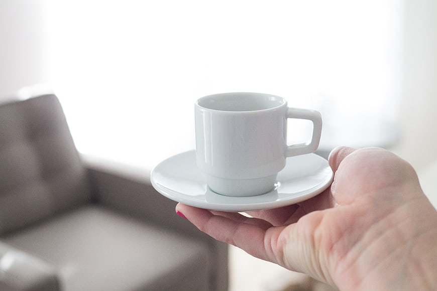 Hand holding white coffee cup on saucer with bright background