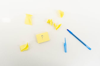 Yellow sticky note with question mark and blue pen on white background
