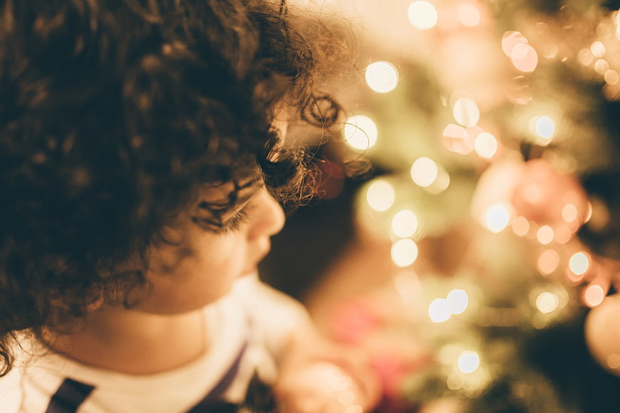 Toddler with curly hair looking at Christmas tree lights