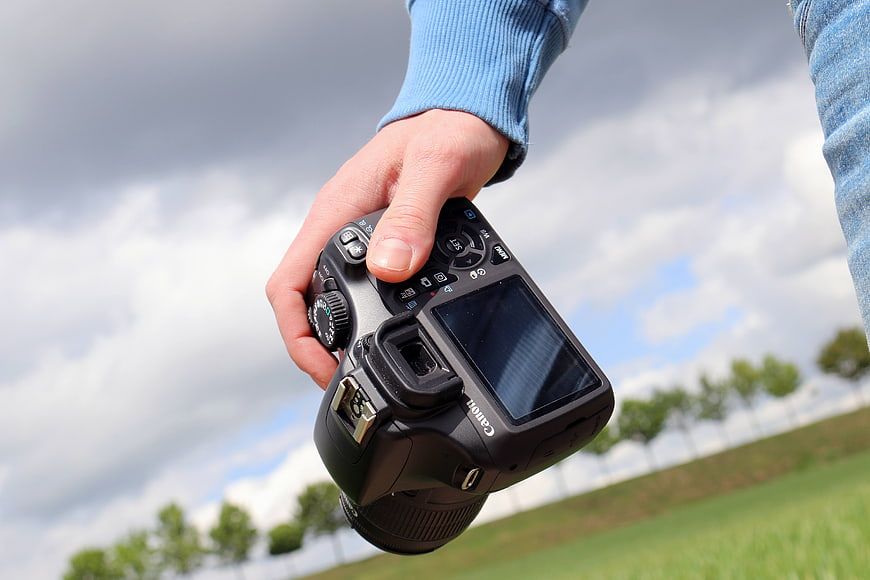 Hand holding DSLR camera outdoors against cloudy sky
