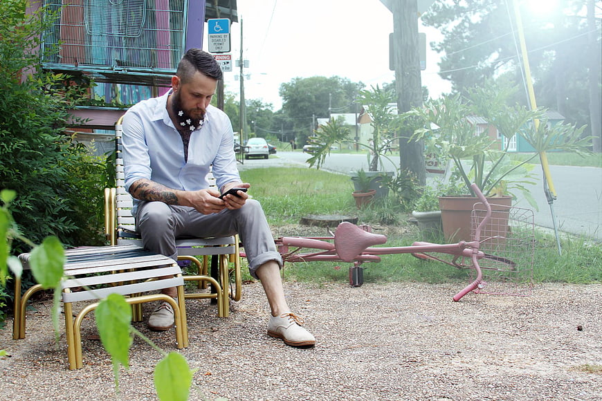 Man with beard sitting on bench using smartphone outdoors