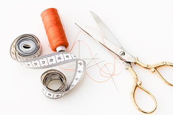 Sewing tools with orange thread, scissors, and measuring tape on white