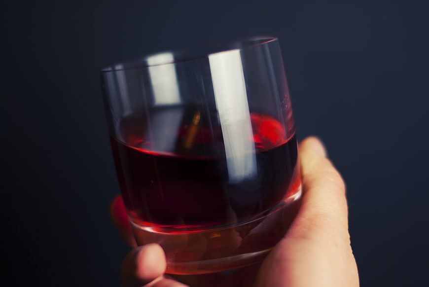 Hand holding glass of red liquid against dark background