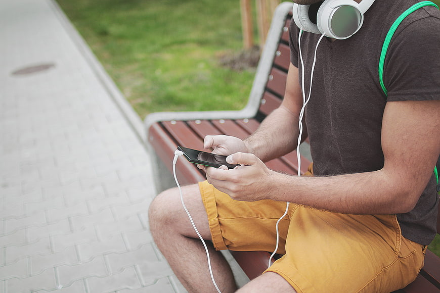 Man listening to music on smartphone with headphones on park bench