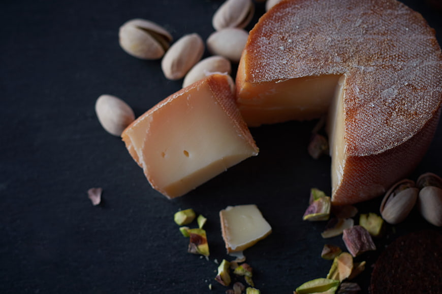 Artisanal cheese wheel with pistachios on dark slate background