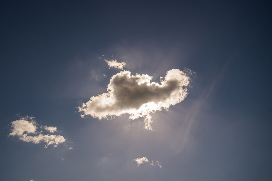 Sun rays shining through a single cloud in blue sky