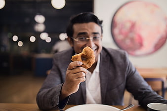 Happy businessman holding donut in modern cafe