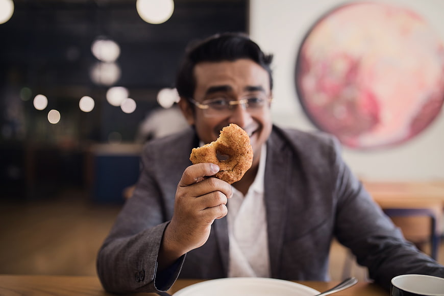 Happy businessman holding donut in modern cafe