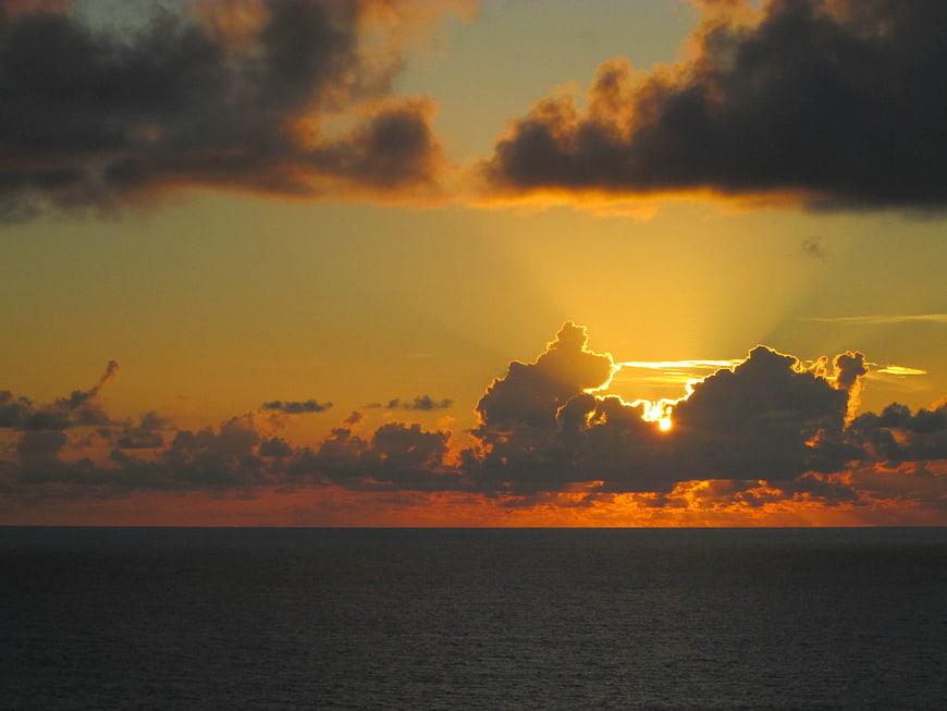 Dramatic Sunset Over Ocean with Golden Sun Rays Through Clouds