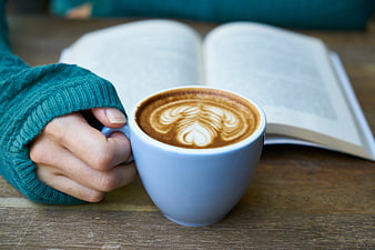 Hand holding latte with book on wooden table