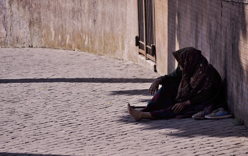 Elderly woman sitting alone on cobblestone street