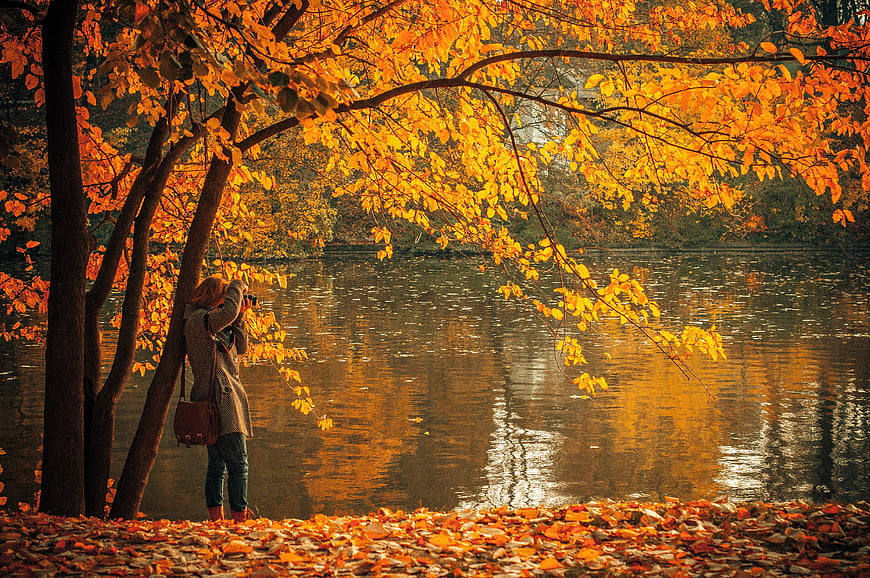 Woman taking photo by lake in autumn foliage