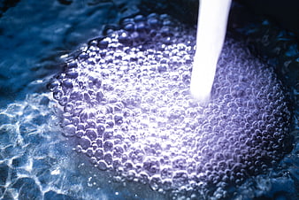 Close-up of flowing water stream creating bubbles in a sink