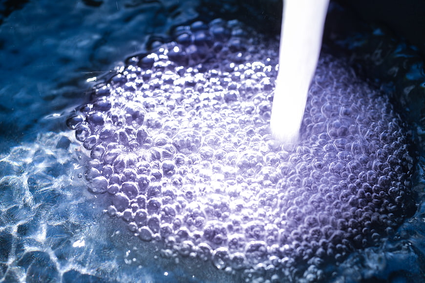 Close-up of flowing water stream creating bubbles in a sink
