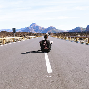 Man sitting on road with mountains in background