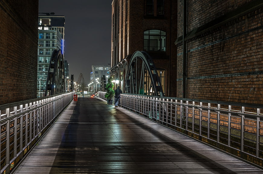 Night view of wooden bridge walkway with brick buildings and city lights