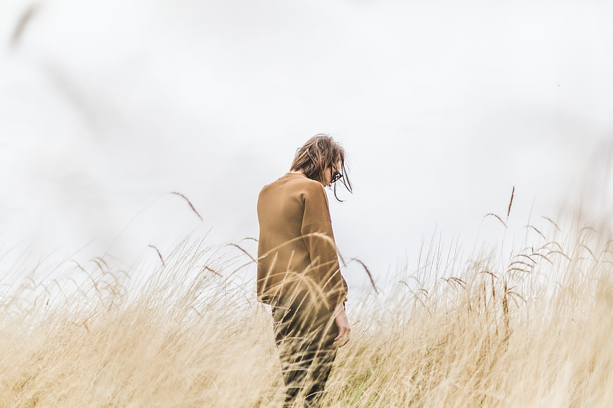 Woman in brown sweater standing in tall dry grass field