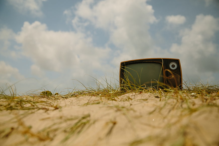 Vintage Television Set on Sandy Dune Under Blue Sky