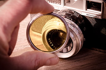 Hand holding yellow filter over vintage Yashica Minister camera lens