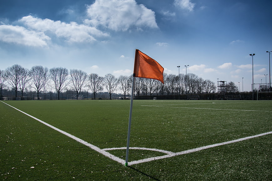 Orange corner flag on green soccer pitch under blue sky