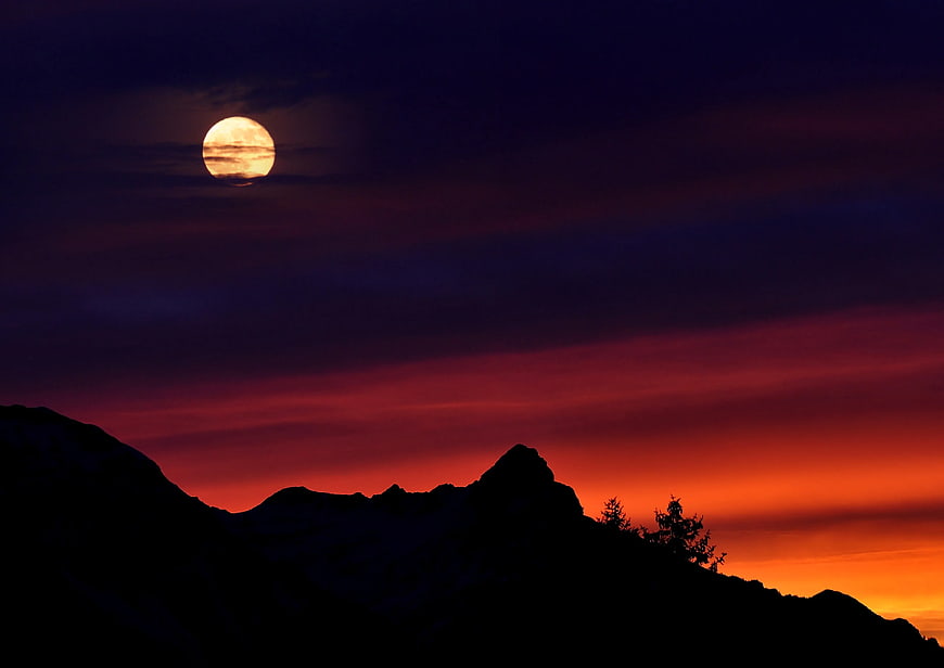 Full Moon Rising Over Silhouetted Mountain Ridge at Sunset