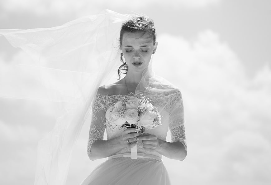 Bride with flowing veil holding bouquet in black and white