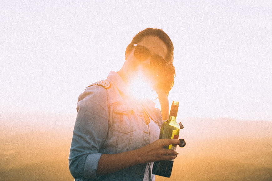 Woman holding wine bottle at sunset with lens flare