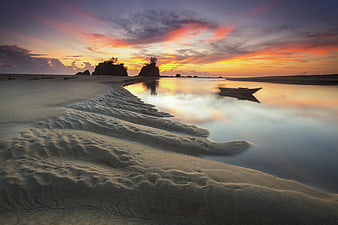 Serene Sunset Beach with Silhouetted Boat and Sand Ripples