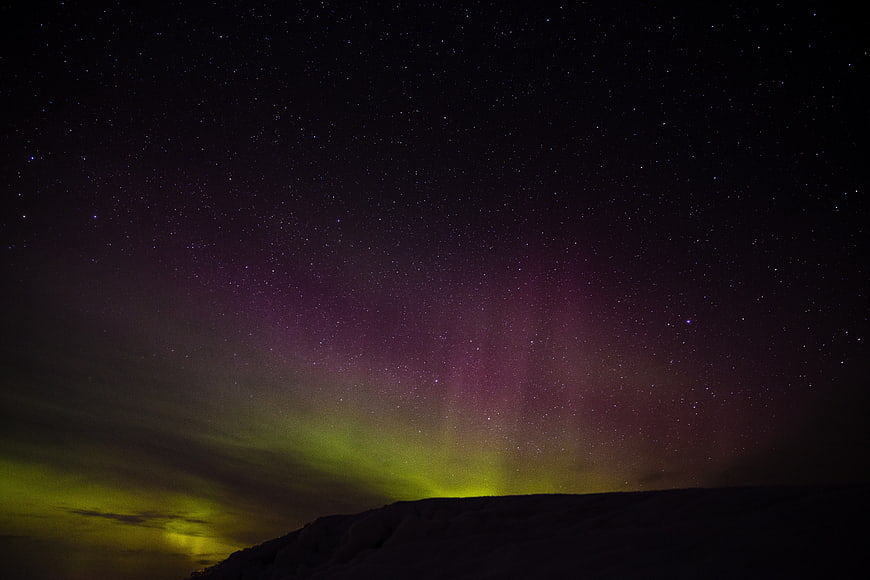 Vivid Purple and Green Aurora Borealis Over Dark Mountain Silhouette