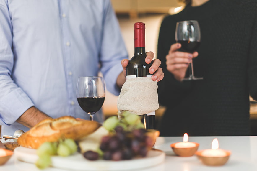 Couple holding wine bottle and glasses with cheese board and candles
