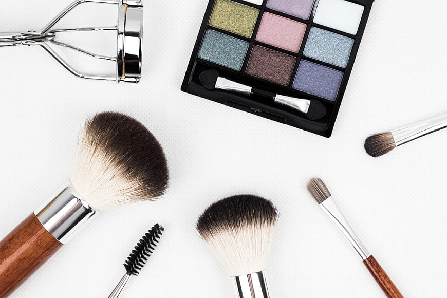 Flat lay of makeup brushes, eyeshadow palette, and eyelash curler on white background