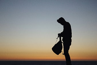 Silhouette of Man with Bag Against Sunset Sky