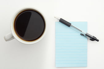 Top view of coffee cup and blue notepad with pen on white background